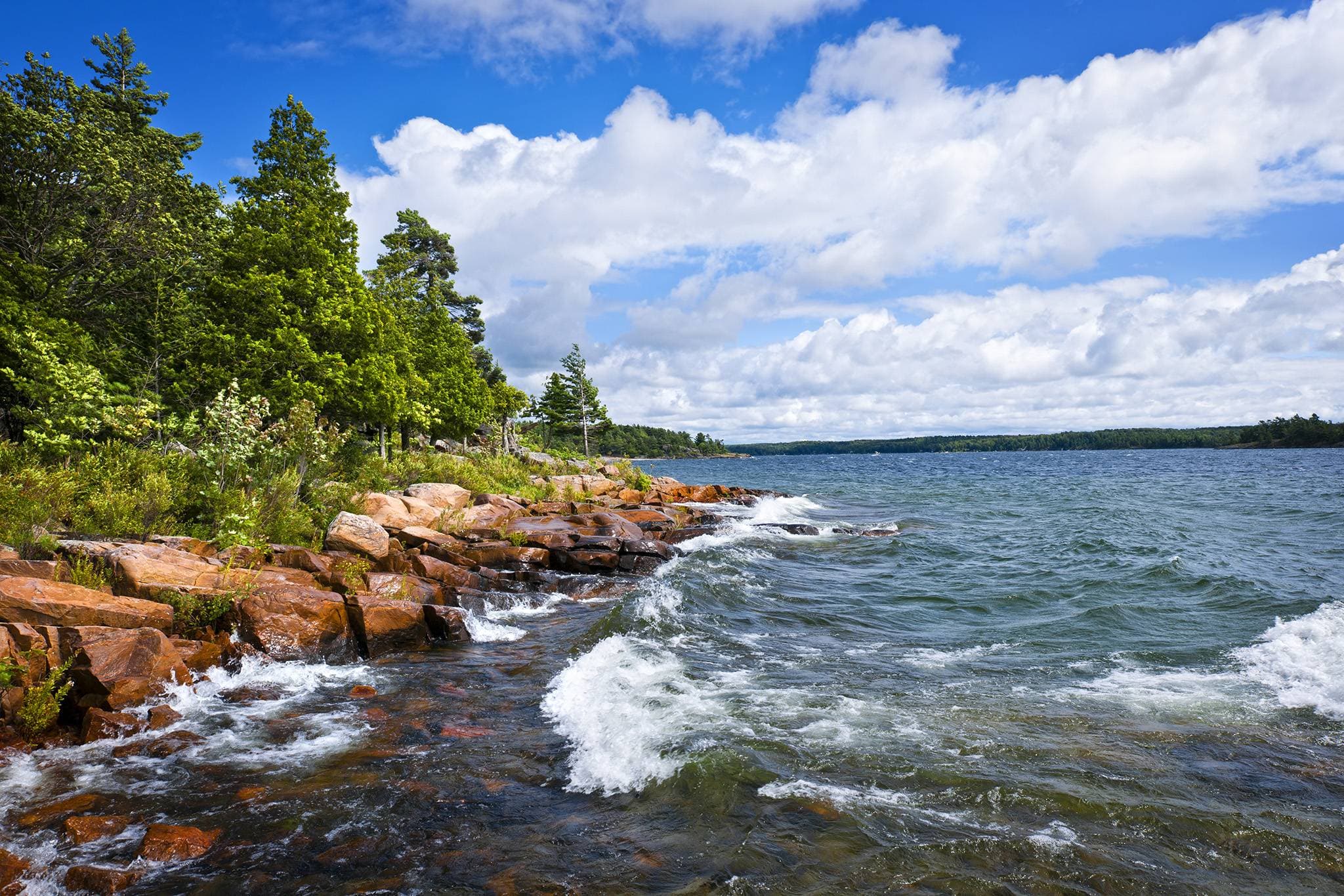 Waves breaking on the pink granite shoreline at Killbear Provincial Park under a blue sky