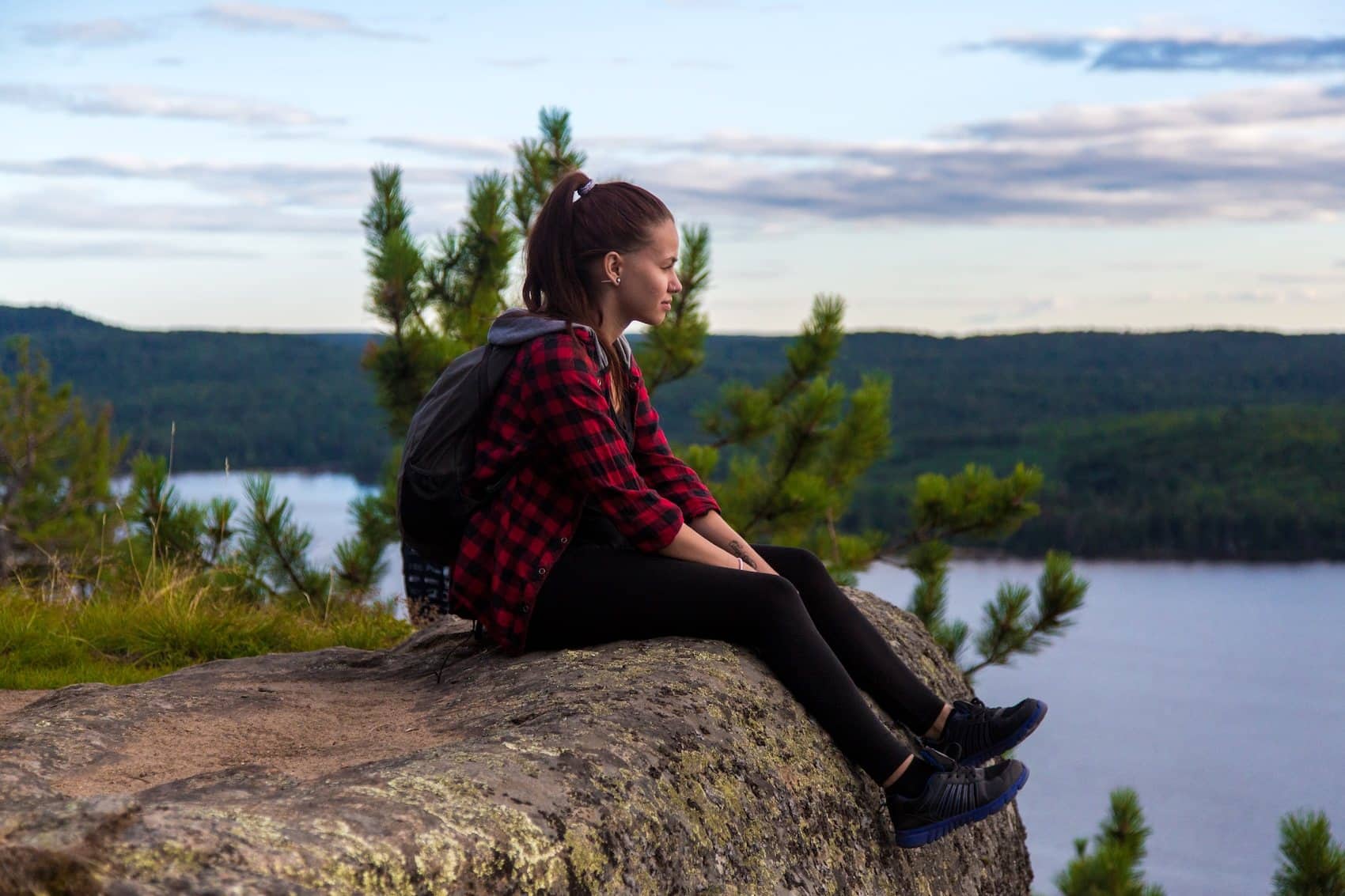 A Parkbus passenger sitting on a rock above a lake in Algonquin Park